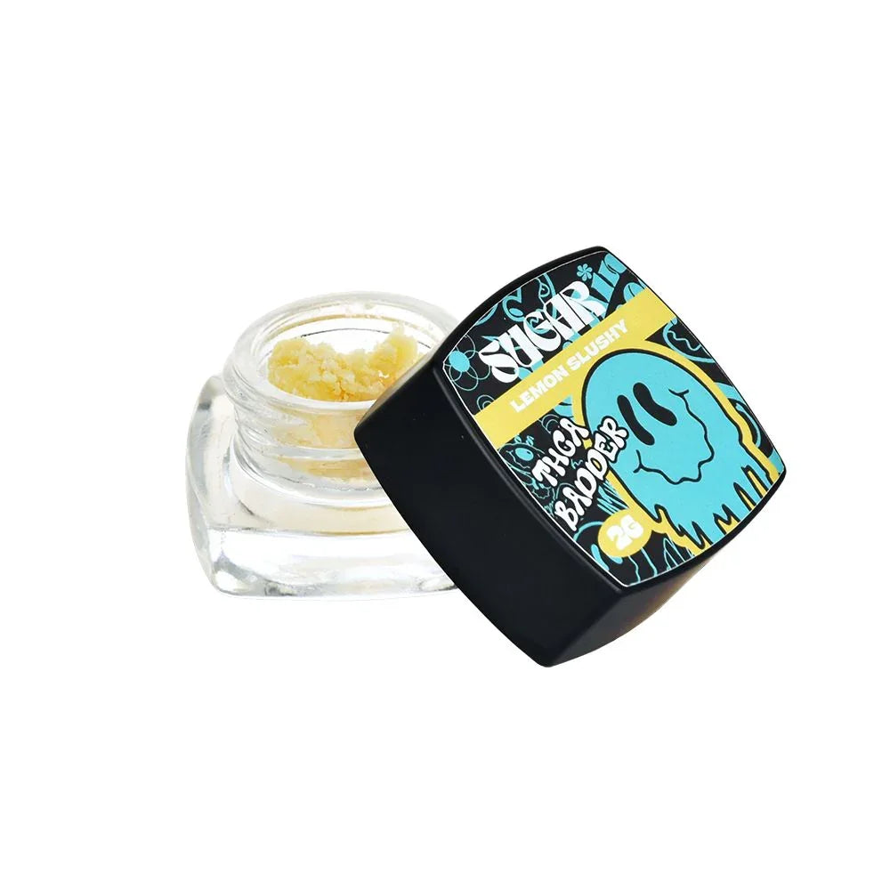 A small glass jar with a black lid, labeled "Trippy Sugar THCa Badder 2G | 5-Pack" by Trippy Sugar, features blue and yellow graphics and contains yellow, crumbly hemp concentrate ideal for dabbing.