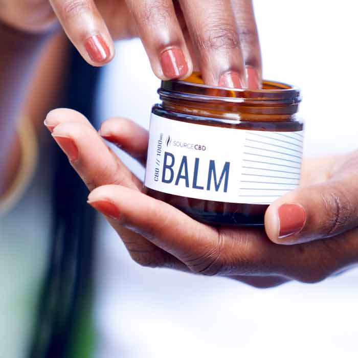 Young woman holding and using Source CBD Balm