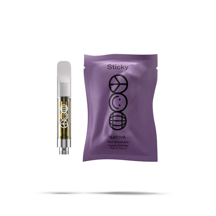 A QWIN Puffy Sticky THCA Cartridge (1.1G) with yellow liquid stands beside a sealed purple pouch labeled Sticky Sativa Blue Slurps, both featuring black circular geometric designs, set against a white background.