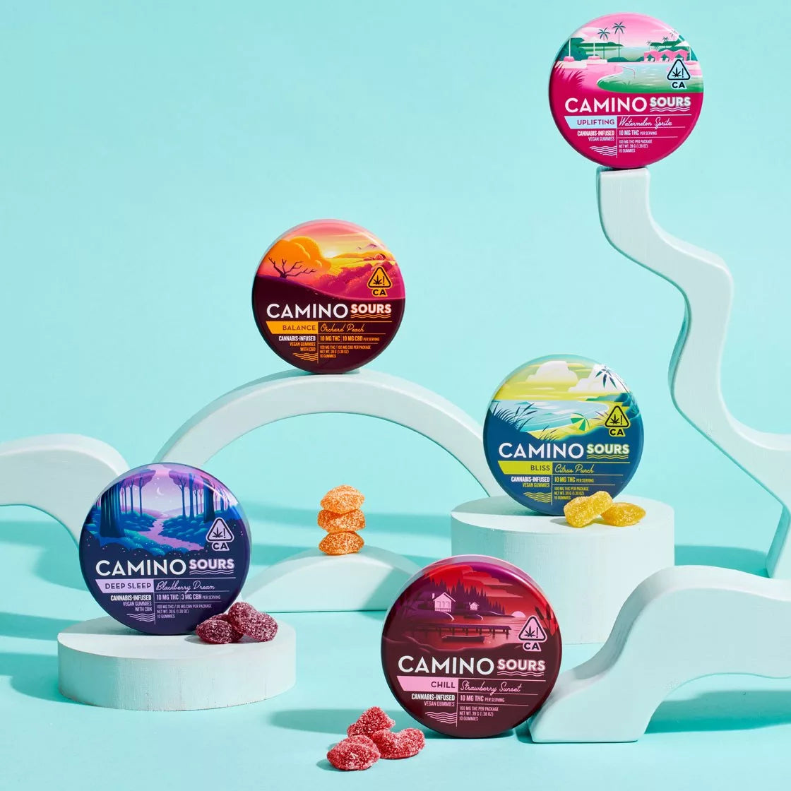 An open pink tin of Kiva Confections Camino Gummies Delta 9 THC 5mg 20ct shows three red, square gummies beside it. The round tin features a poolside illustration and THC warning symbols.